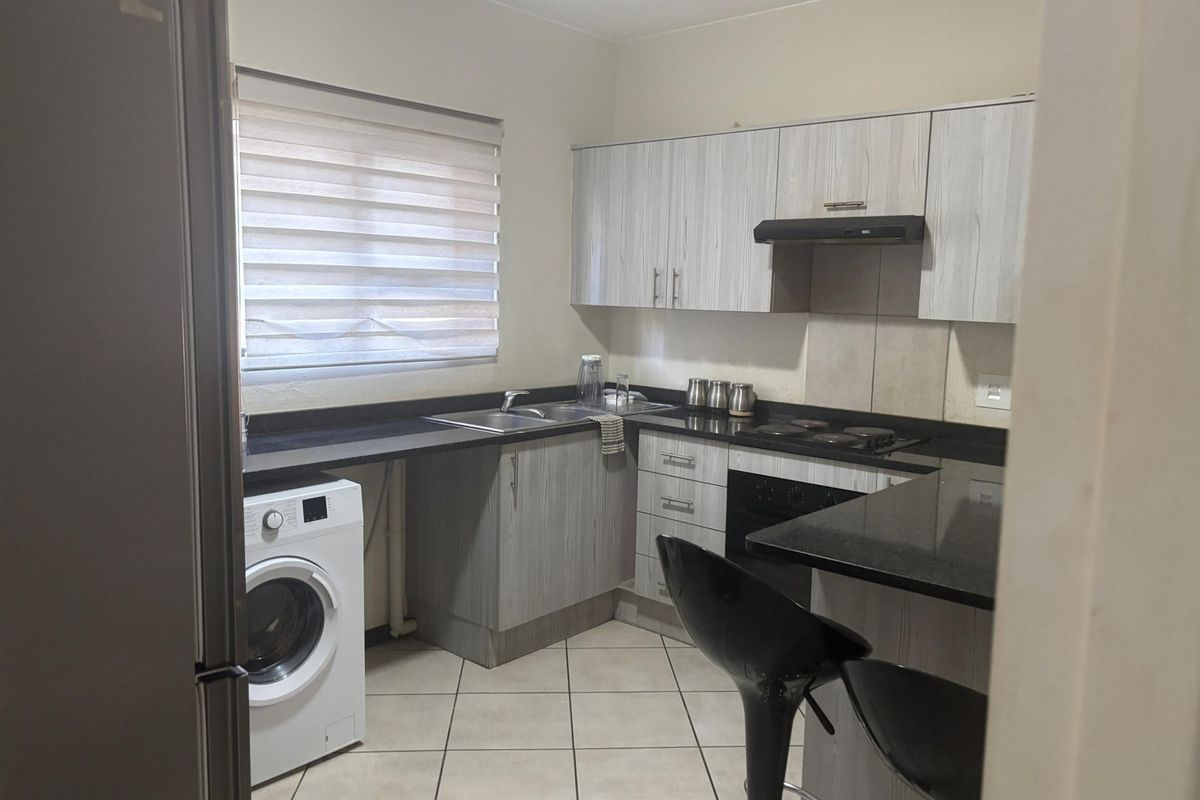 A functional kitchen featuring light wood-grain cabinetry, dark granite countertops, integrated appliances, and tiled flooring with a window providing natural light.
