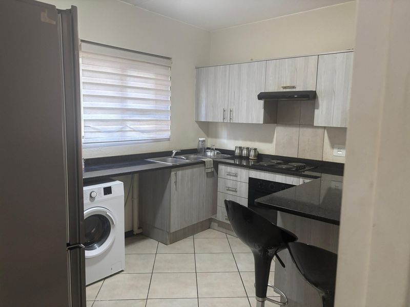 A functional kitchen featuring light wood-grain cabinetry, dark granite countertops, integrated appliances, and tiled flooring with a window providing natural light.