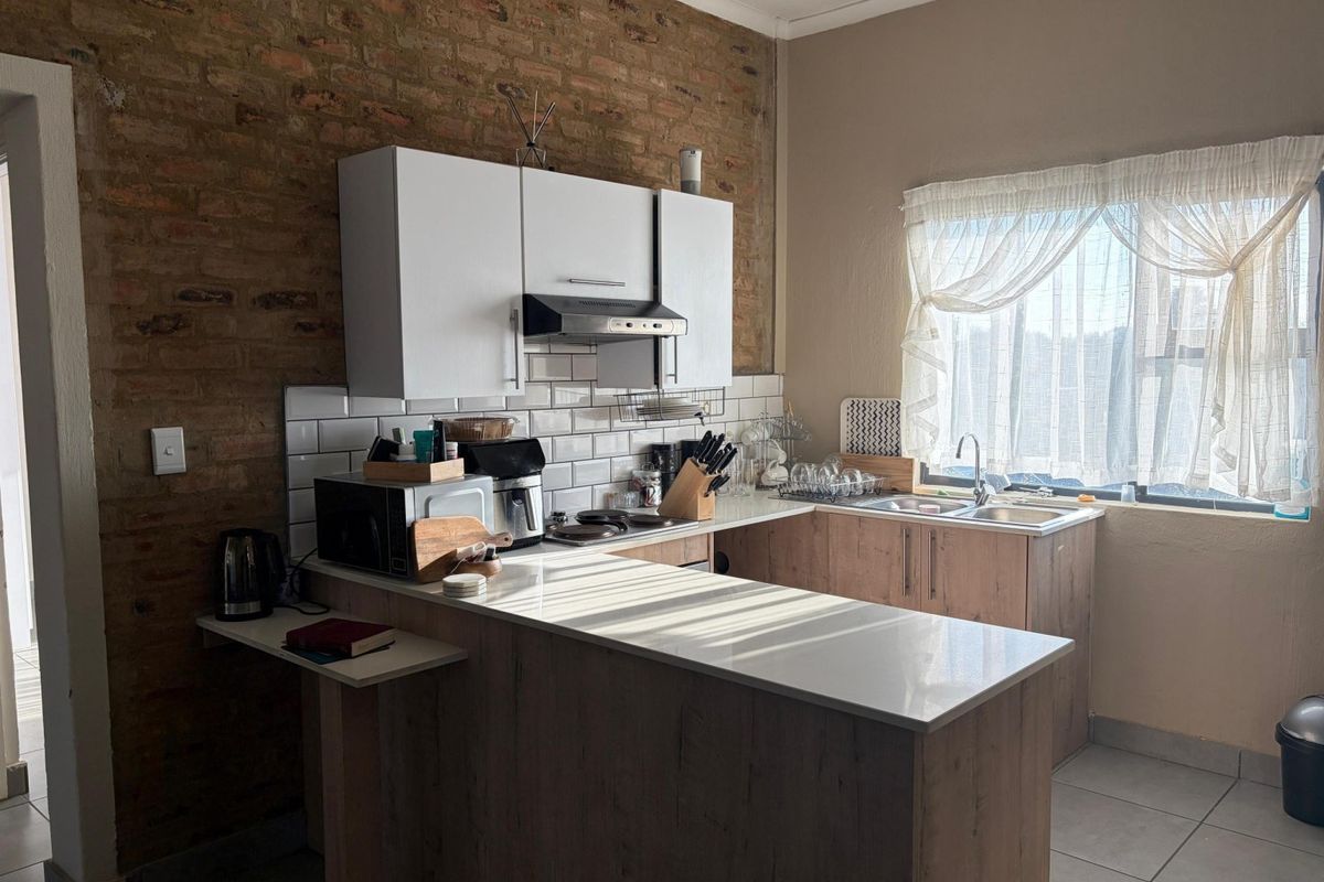 A functional kitchen featuring exposed brick walls, subway tile backsplash, modern cabinetry, stone countertops, and a convenient breakfast bar area.