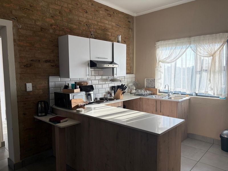 A functional kitchen featuring exposed brick walls, subway tile backsplash, modern cabinetry, stone countertops, and a convenient breakfast bar area.