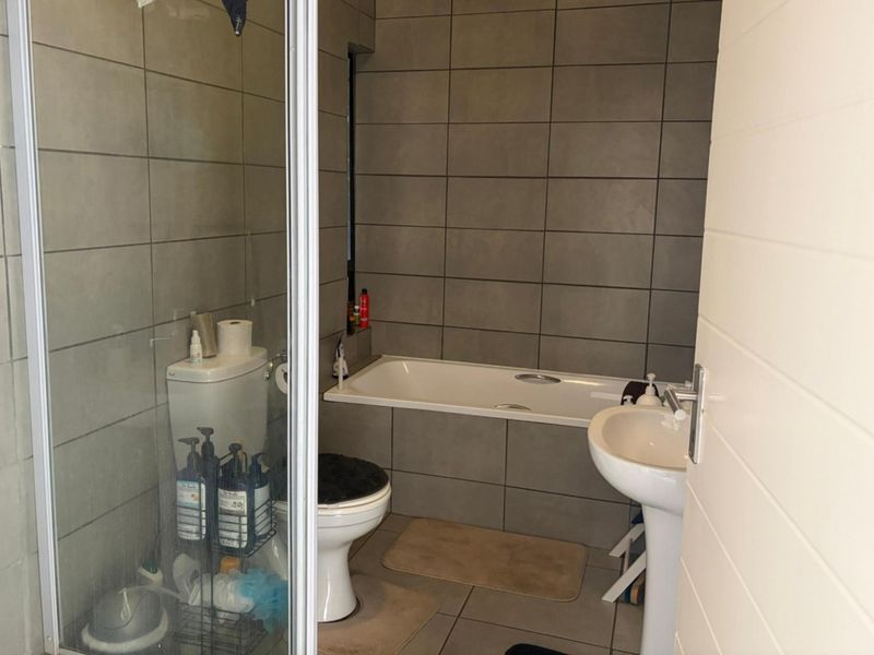 A functional bathroom featuring a shower enclosure, bathtub, pedestal basin, and toilet with neutral grey wall and floor tiling.