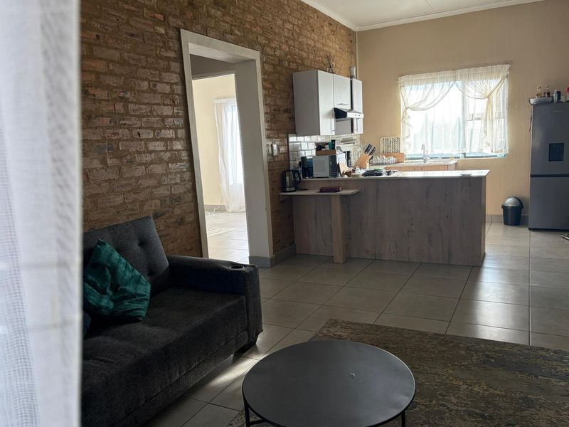 Open-plan living and kitchen area featuring an exposed brick feature wall, tiled flooring, and a functional kitchen island with cabinetry.