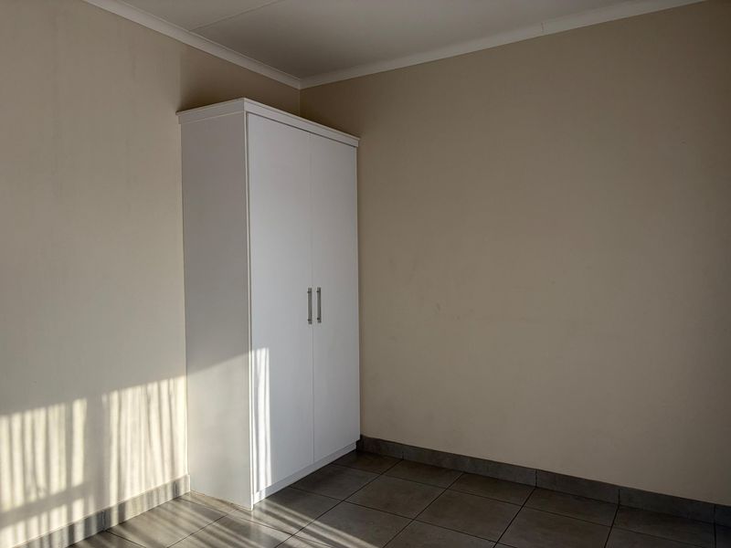 A clean, minimalist bedroom featuring neutral walls, tiled flooring, and a white built-in wardrobe.