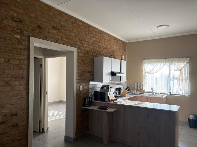 Kitchen featuring an exposed brick feature wall, built-in cabinetry, tiled backsplash, and a breakfast counter overlooking the living area.