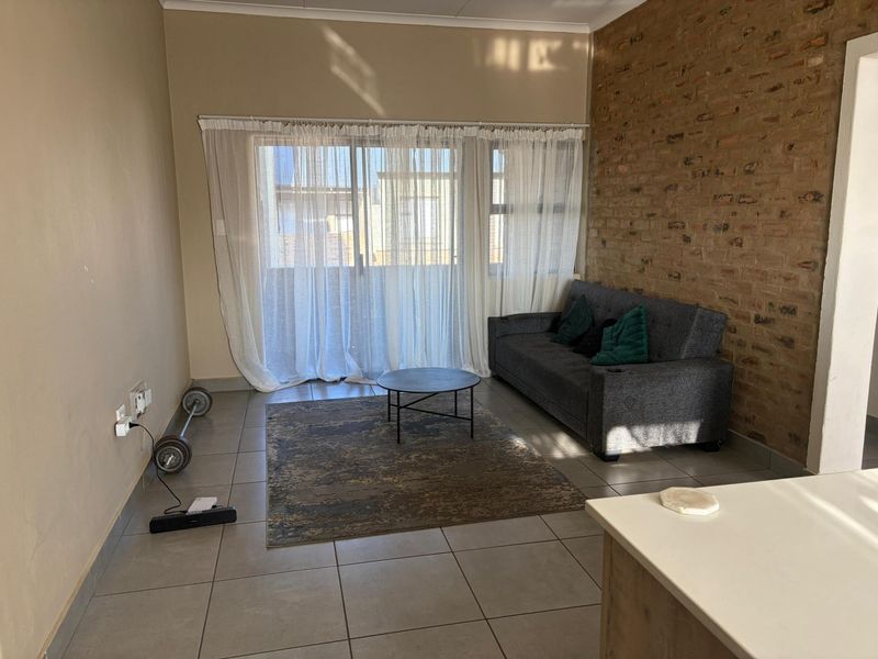 A living room featuring an exposed brick wall, tiled flooring, and a large sliding glass door providing natural light.