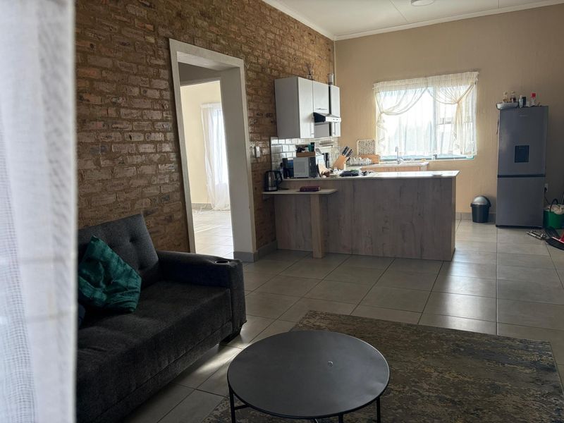 Open plan living and kitchen area featuring an exposed brick feature wall, tiled flooring, and a functional kitchen island with cabinetry.