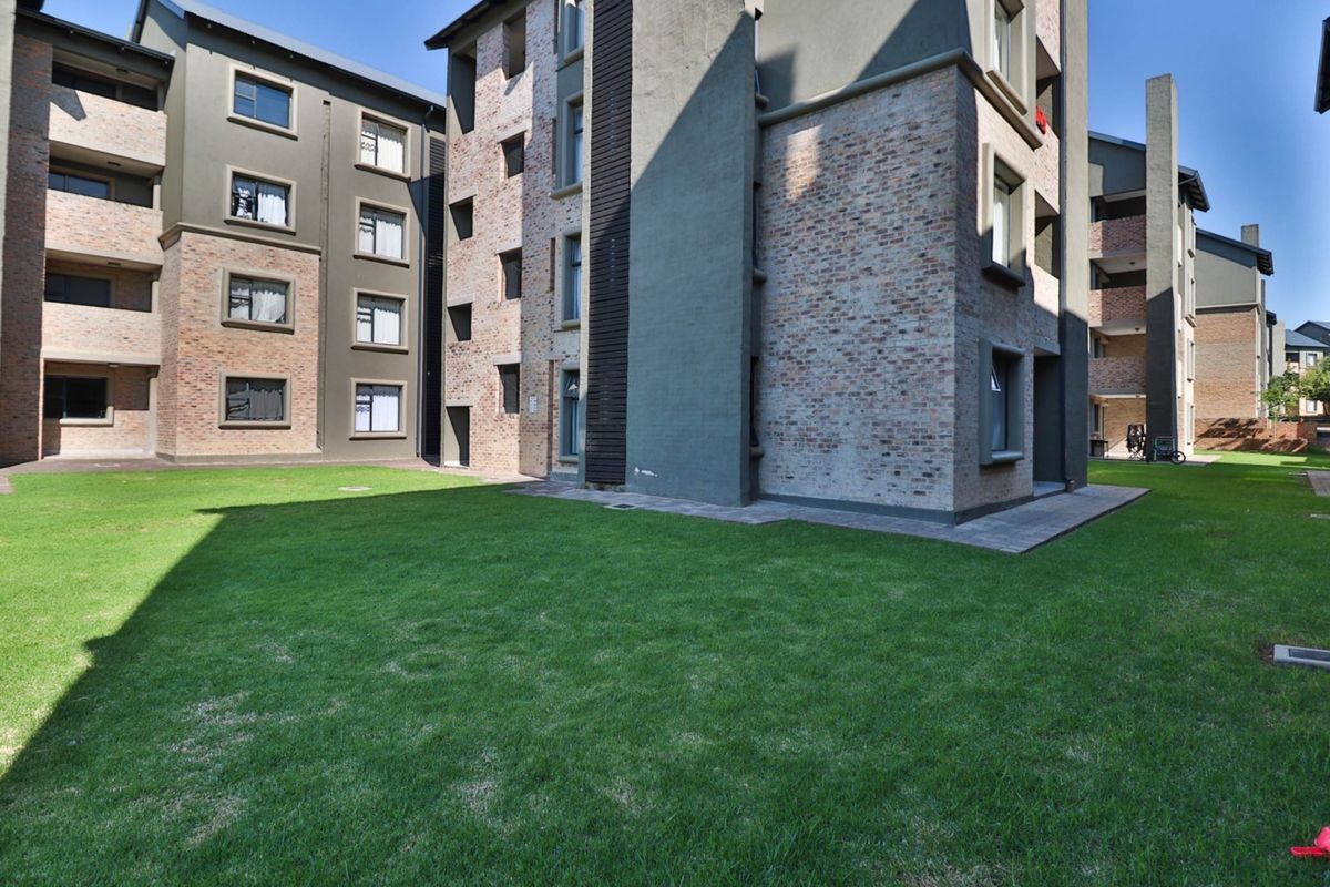 A view of the rear exterior of a modern apartment complex featuring brick and rendered facades with a well-maintained communal lawn area.