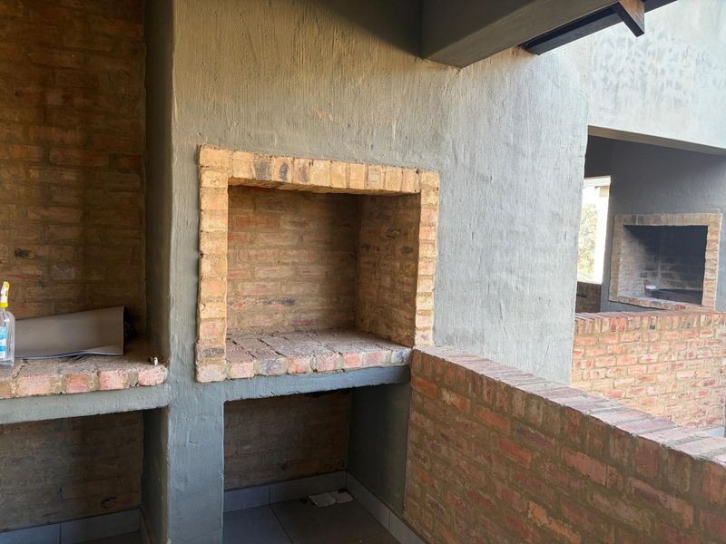 An outdoor patio area featuring a built-in brick braai and masonry walls, currently in an unfinished state requiring final finishes and cleaning.