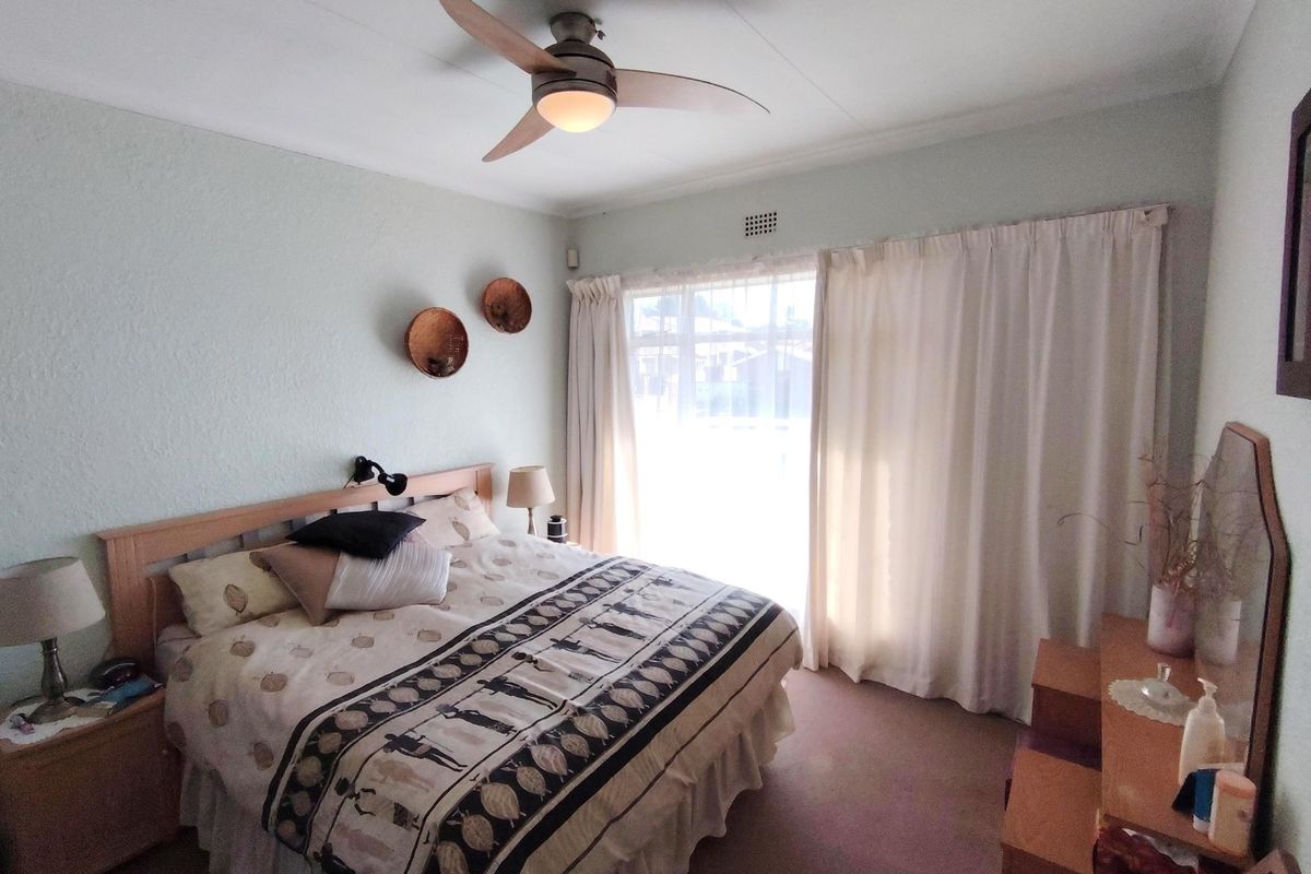 A bedroom featuring a ceiling fan, carpeted flooring, and a large sliding glass door with curtains providing natural light.