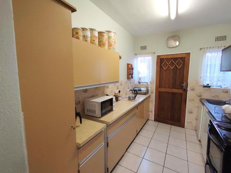 A functional kitchen featuring dated cabinetry, tiled backsplash, and tiled flooring, offering a practical layout with potential for modern renovation.