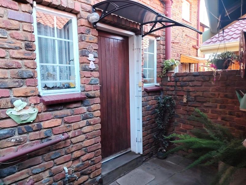 A private rear courtyard featuring exposed brick walls, a timber entrance door with a protective canopy, and paved flooring.