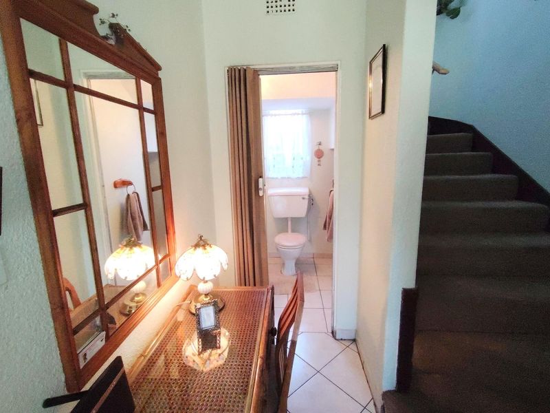 A hallway area featuring tiled flooring, a staircase leading to the upper level, and access to a small bathroom with a folding door.
