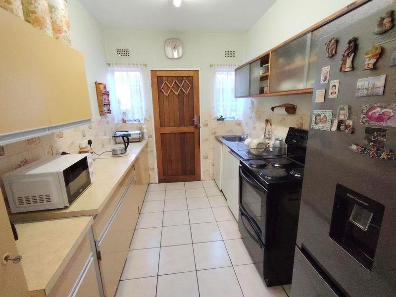 A functional galley-style kitchen featuring laminate countertops, built-in cabinetry, a tiled backsplash, and ceramic floor tiles.