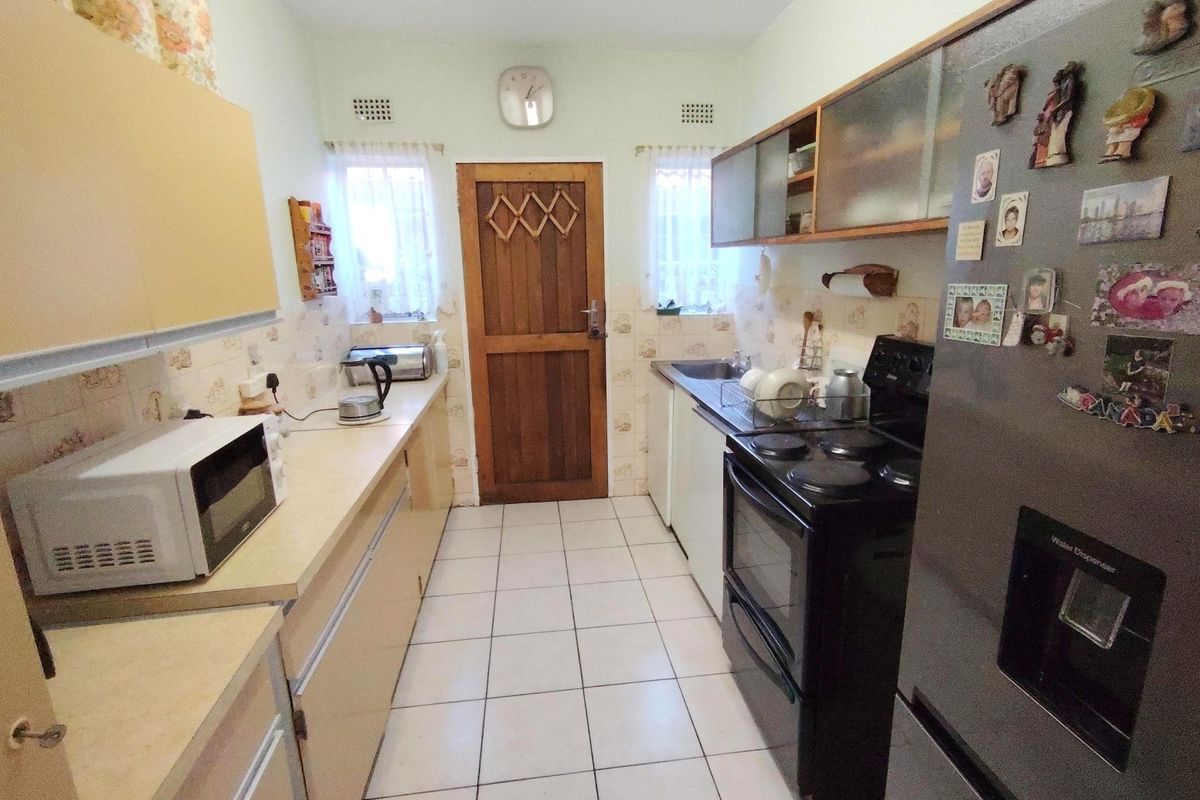 A functional galley-style kitchen featuring laminate countertops, built-in cabinetry, a tiled backsplash, and ceramic floor tiles.