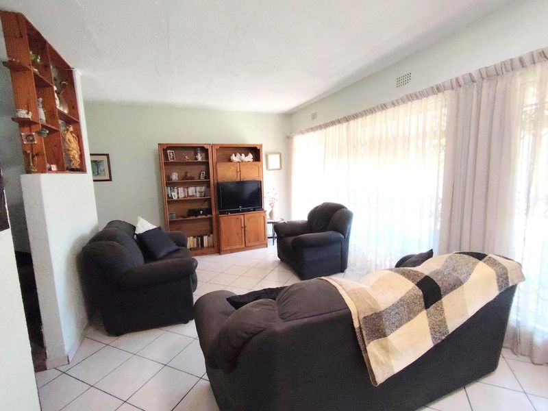 A spacious living room featuring tiled flooring and built-in shelving, offering a functional layout with natural light through large window treatments.