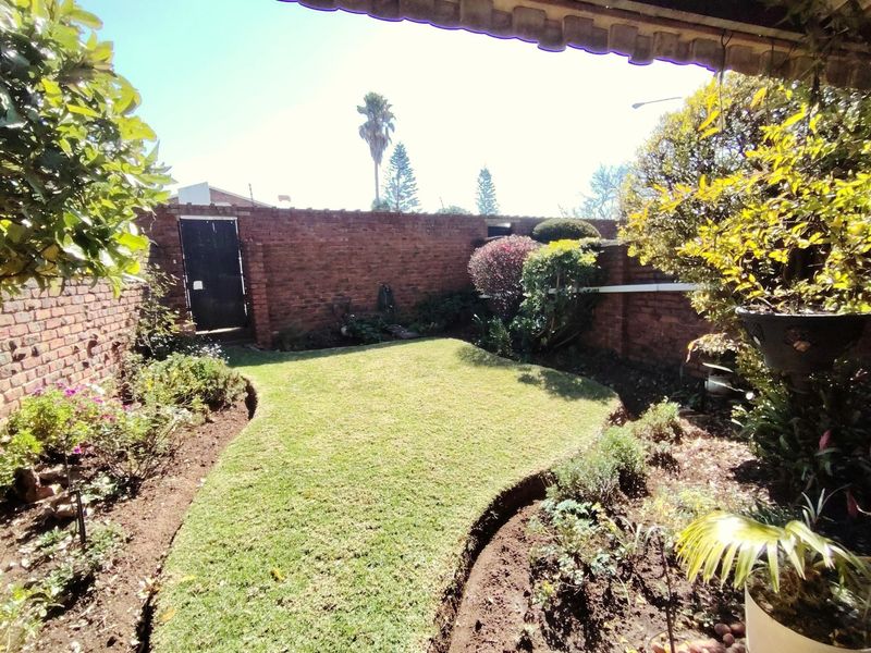 A private rear garden featuring a well-maintained lawn, established garden beds, and a brick boundary wall with a secure pedestrian gate.