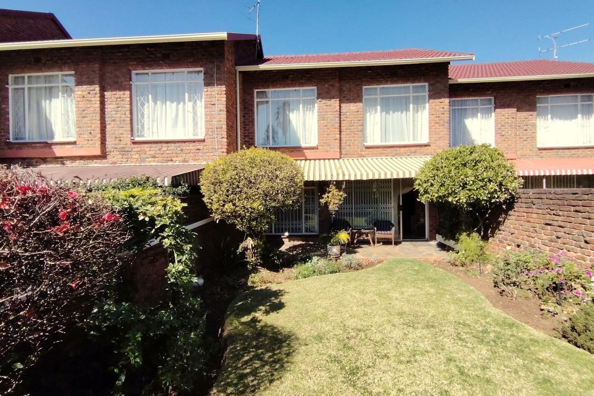 Rear view of the townhouse featuring a face brick facade, a private garden with a lawn, and a paved patio area with a retractable awning.