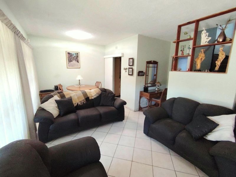 A spacious living room featuring tiled flooring and a built-in wooden display shelf, offering a functional layout for relaxation and dining.