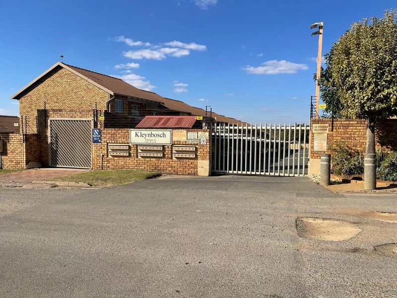 Front entrance view of Kleynbosch apartment complex featuring a secure gated access point, brick facade, and integrated post boxes.