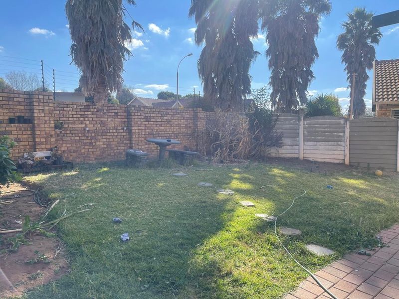 A private rear garden featuring a lawn area, paved path, and perimeter brick and concrete boundary walls with electric fencing.