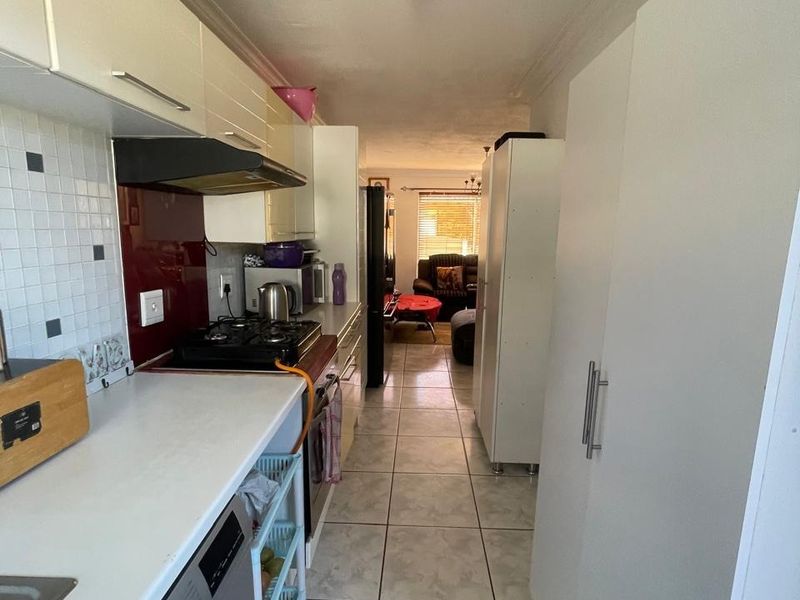 A functional galley-style kitchen featuring white cabinetry, a gas hob with extractor, tiled backsplash, and integrated laundry connections, leading into the living area.