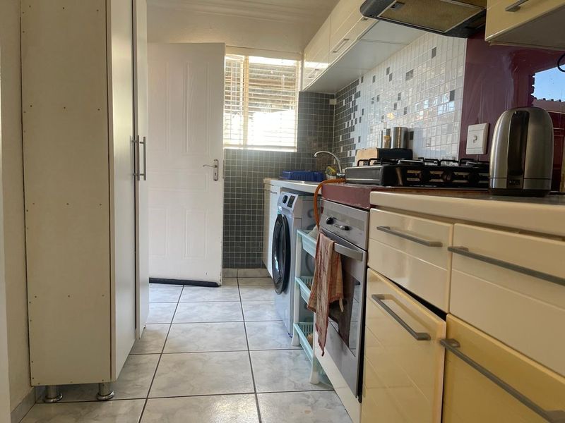 Compact kitchen featuring built-in cabinetry, gas hob, electric oven, extractor fan, and tiled backsplash with direct access to an exterior door.