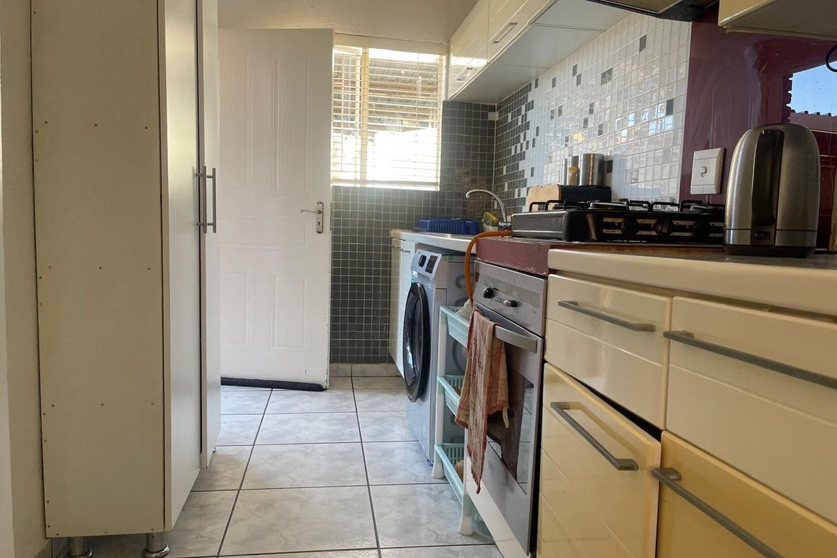 Compact kitchen featuring built-in cabinetry, gas hob, electric oven, extractor fan, and tiled backsplash with direct access to an exterior door.