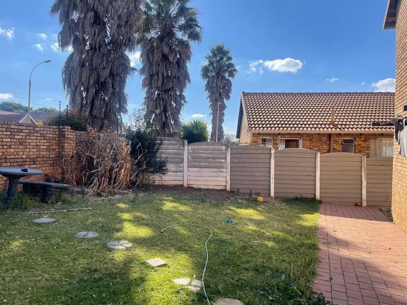 A private rear garden featuring a lawn, paved walkway, and a combination of brick and precast concrete boundary walls.