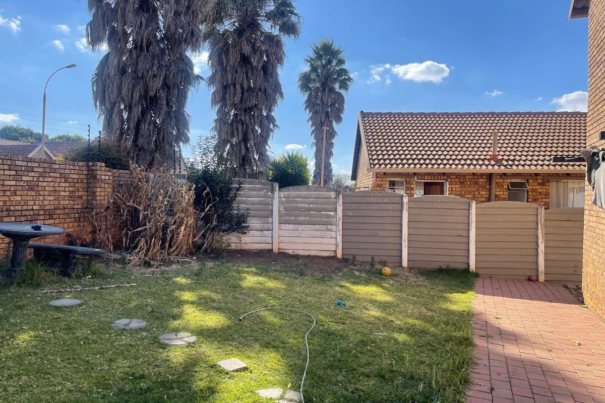 A private rear garden featuring a lawn, paved walkway, and a combination of brick and precast concrete boundary walls.