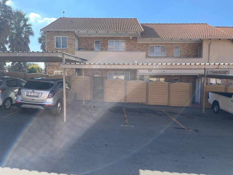 Front view of a brick apartment complex featuring a covered carport parking area and secure fencing.
