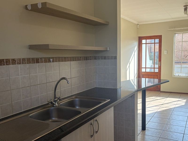 Open plan kitchen and living area featuring granite countertops, double sink, tiled flooring, and direct access to an outdoor balcony through a timber door.