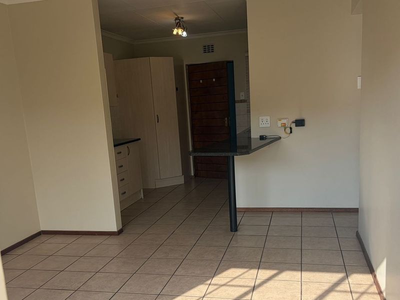 An open-plan living and kitchen area featuring tiled flooring, a breakfast bar, and built-in cabinetry, offering a functional and versatile space.