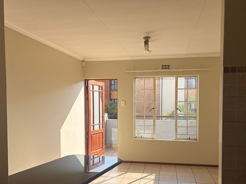 An open-plan living area featuring tiled flooring, a timber door leading to a balcony, and a granite countertop, presenting a clean, vacant space.