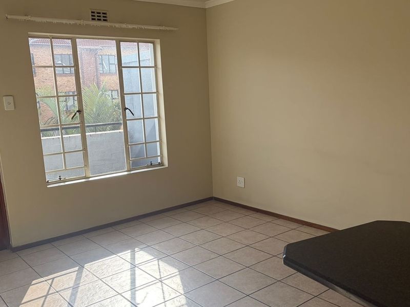 An empty living area featuring tiled flooring, a timber door, and a window with security bars, offering a blank canvas for interior design.