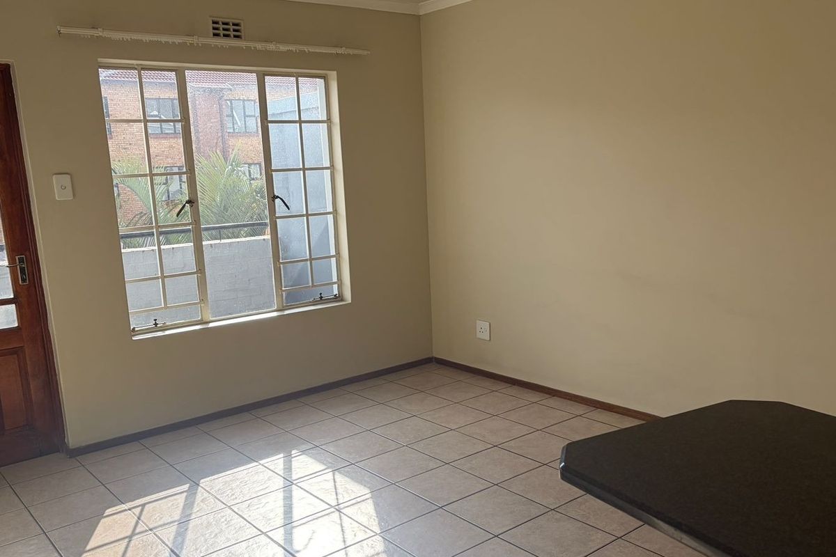 An empty living area featuring tiled flooring, a timber door, and a window with security bars, offering a blank canvas for interior design.