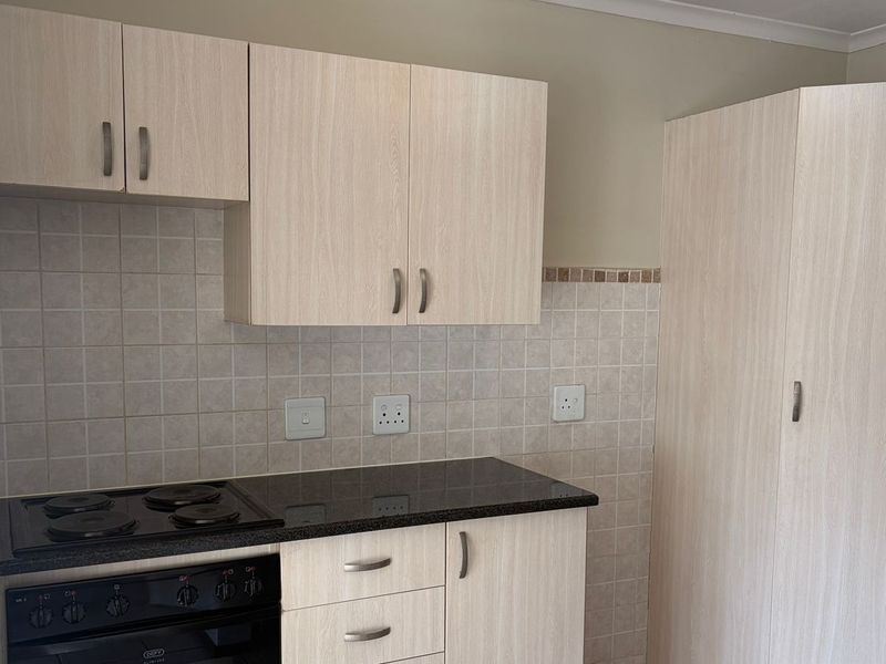 A clean, functional kitchen featuring light wood-finish cabinetry, dark laminate countertops, a built-in electric oven and hob, and a tiled backsplash.