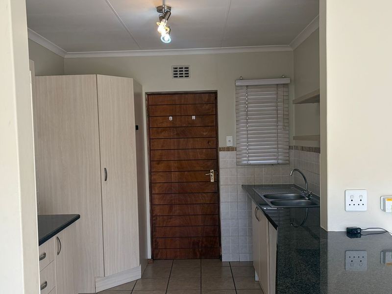A functional kitchen area featuring granite countertops, double basin sink, built-in cabinetry, and tiled flooring, offering a clean and practical workspace.