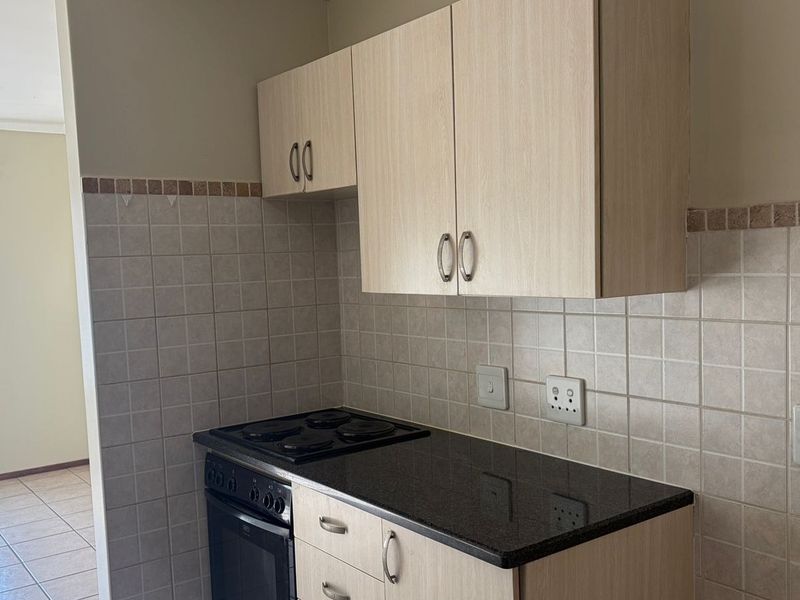 A compact kitchen featuring light wood-finish cabinetry, a black granite countertop, and a built-in electric stove with oven.
