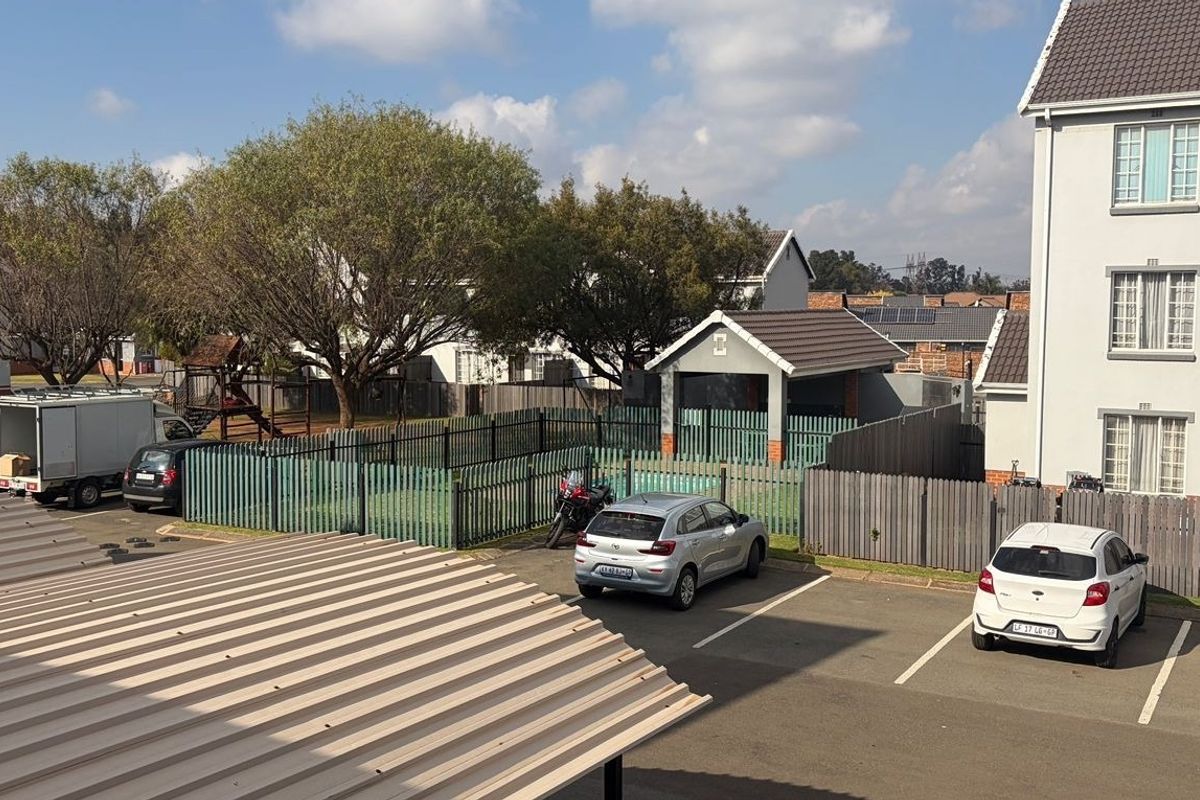 An elevated view of the apartment complex grounds, featuring a paved parking area, metal perimeter fencing, and a communal outdoor space.