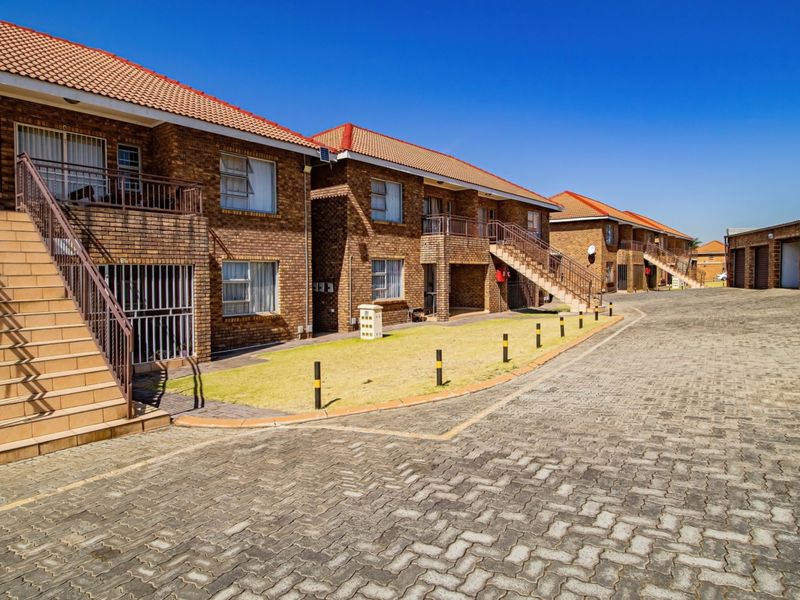 Exterior view of a multi-unit apartment complex featuring face brick construction, tiled roofs, paved driveway, and external staircases leading to upper-level balconies.