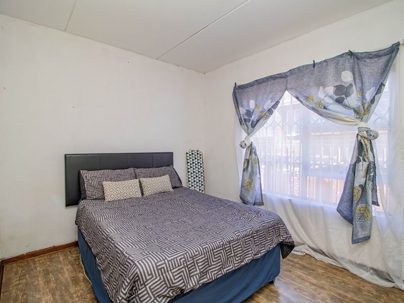 A bedroom featuring laminate flooring and a window fitted with a security gate, requiring minor cosmetic updates to the walls and ceiling.