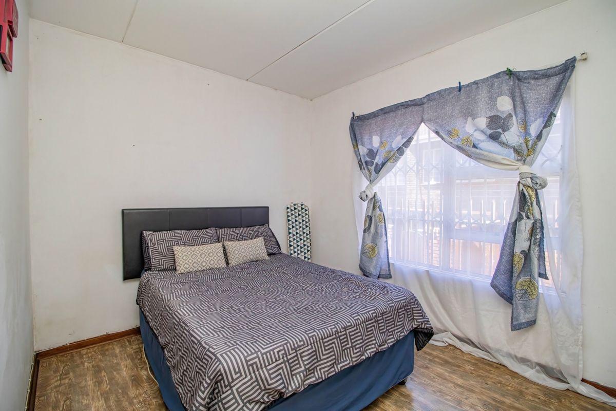 A bedroom featuring laminate flooring and a window fitted with a security gate, requiring minor cosmetic updates to the walls and ceiling.