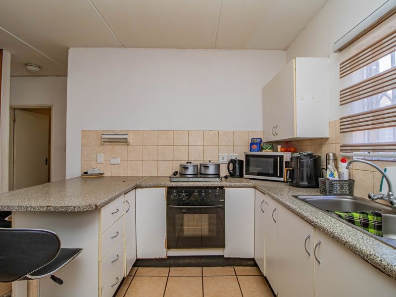 A functional kitchen featuring laminate countertops, built-in cabinetry, a stainless steel sink, and a built-in oven with hob, finished with tiled backsplash and flooring.