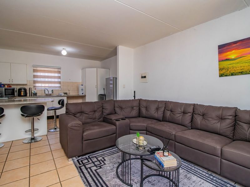 Open-plan living area featuring a functional kitchen with breakfast bar, tiled flooring, and neutral finishes, creating a versatile space for daily living.