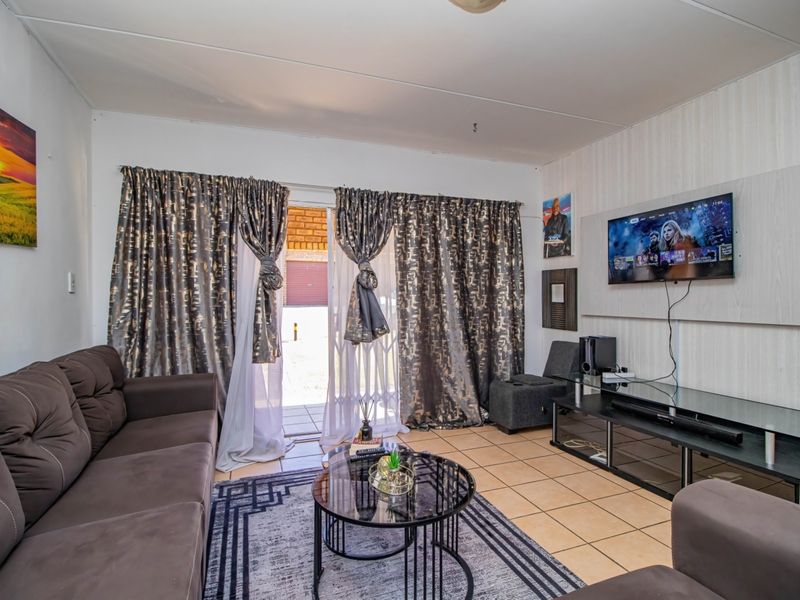 A living room featuring tiled flooring, a wall-mounted TV panel, and a sliding glass door providing access to the exterior.