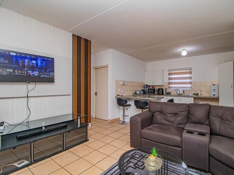 Open plan living area featuring tiled flooring, a functional kitchen with breakfast bar, and a decorative feature wall with wall-mounted television.