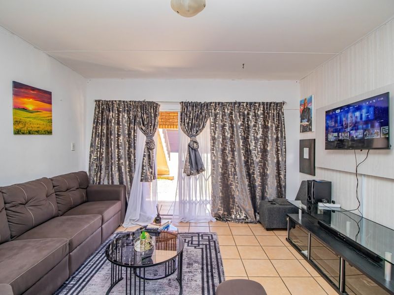A living room featuring tiled flooring and a sliding glass door with security gate providing access to the exterior.