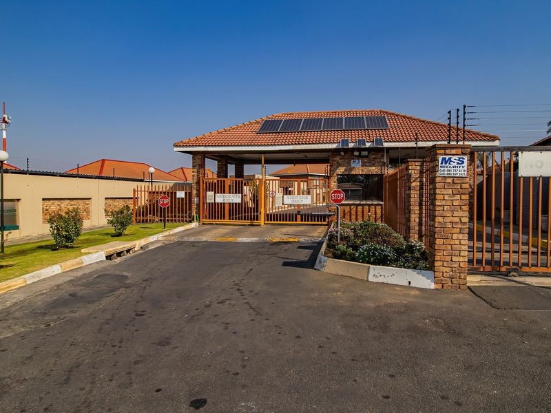 The secure entrance to the apartment complex features a gated access point, brick perimeter walling, electric fencing, and solar panels on the guard house roof.