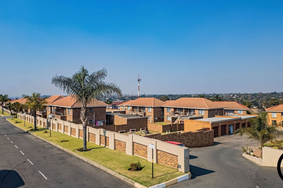 Aerial view of a residential apartment complex featuring brick buildings with tiled roofs, paved driveways, and secure perimeter walling.