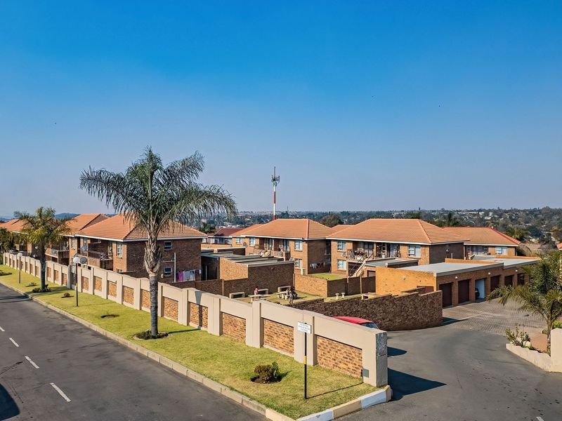 Aerial view of a residential apartment complex featuring brick buildings with tiled roofs, paved driveways, and secure perimeter walling.